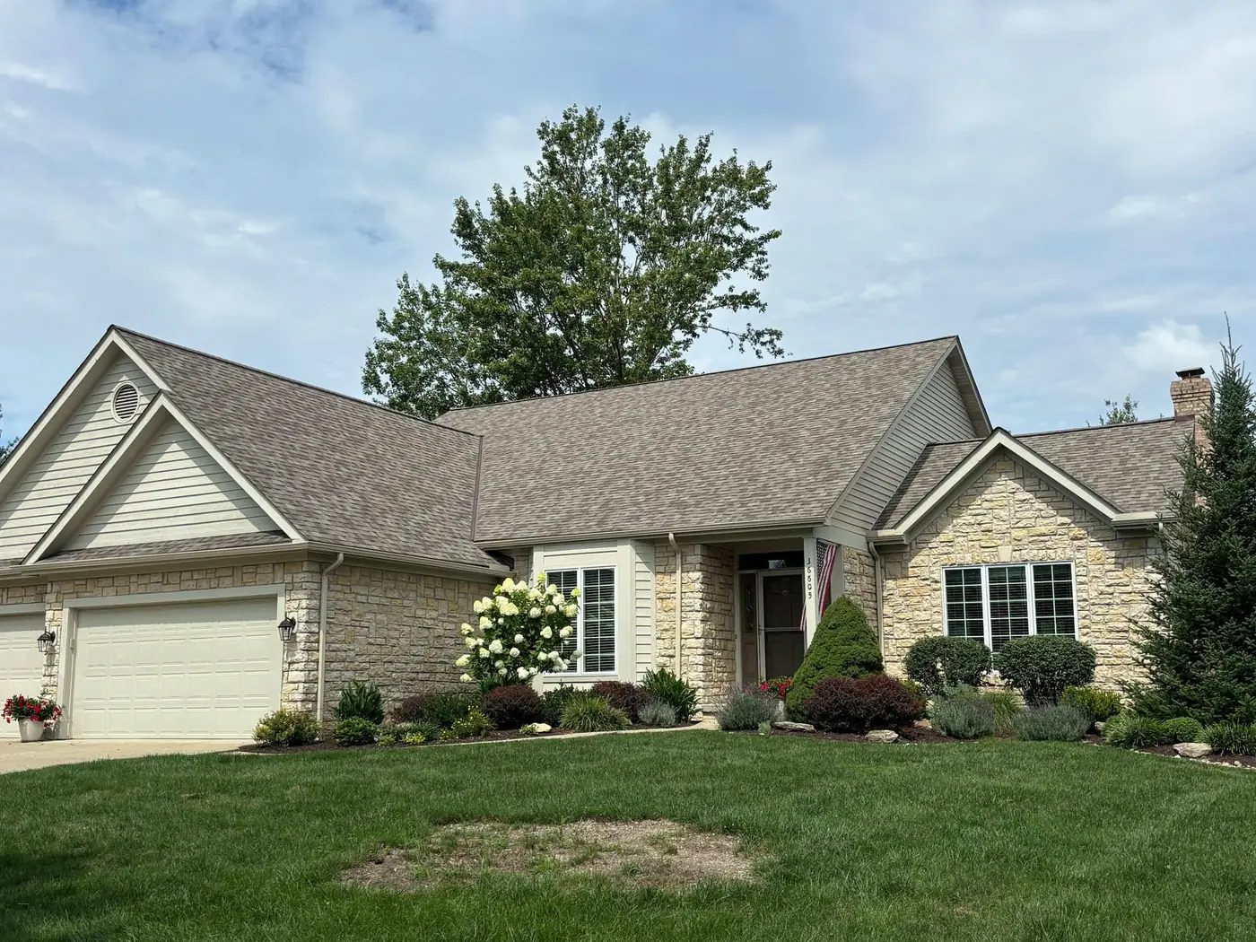 A cream and stone ranch home with a brand-new shingle roof and tidy landscaping.