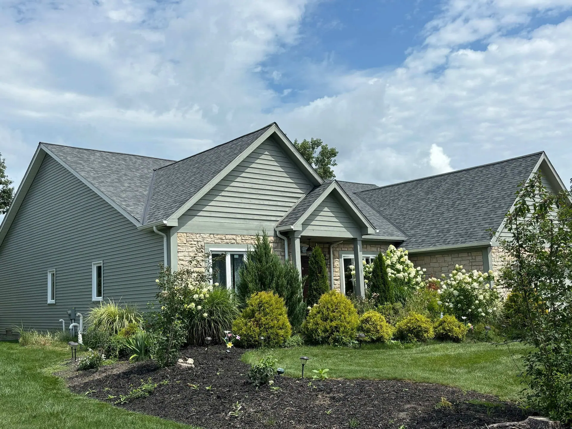 A sage-green home with fresh stone accents and a brand-new dark shingle roof, finished by Predey's Roofing in the Greater Cleveland area.