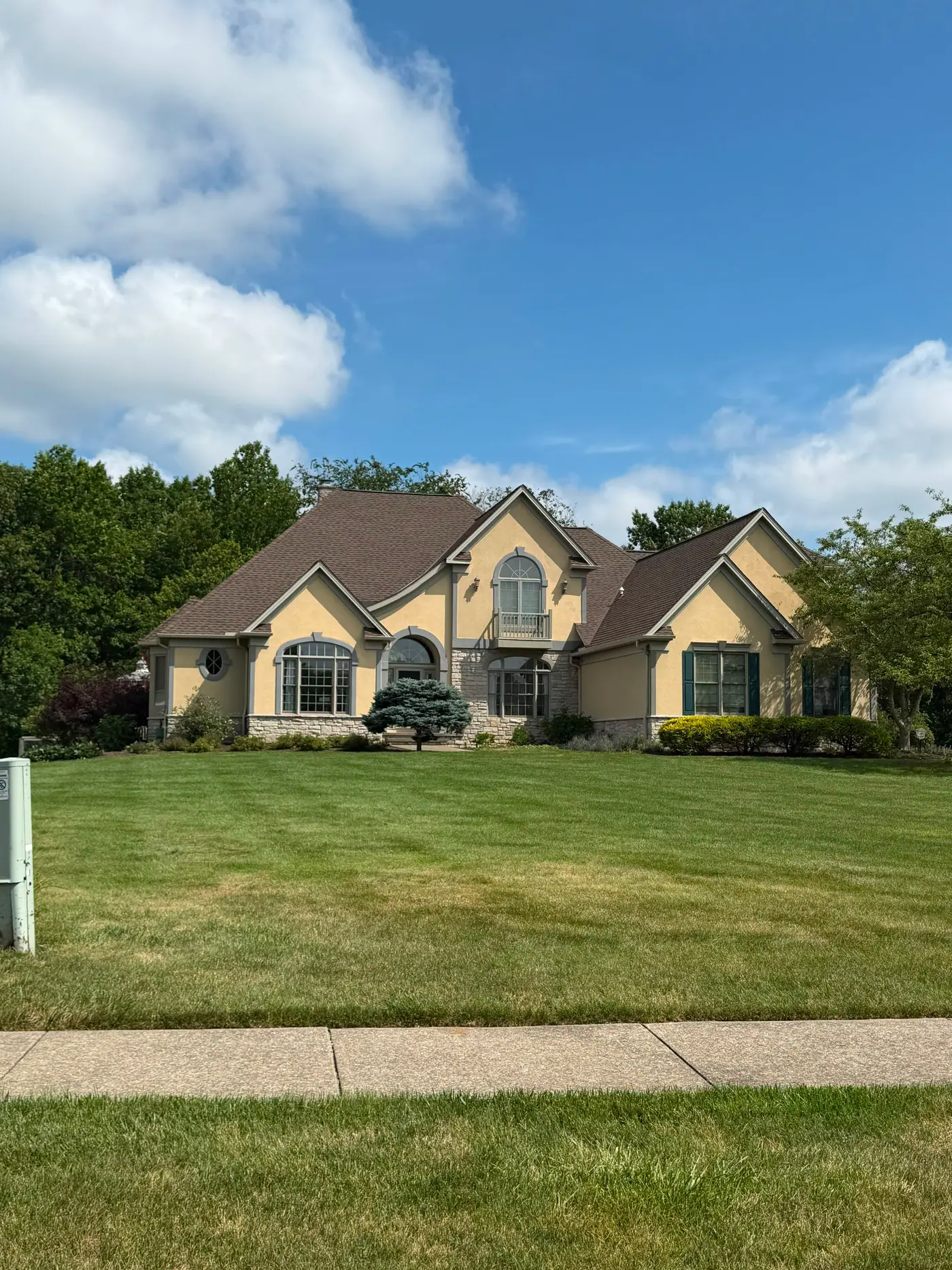 A large stucco and stone home with a full shingle roof, set back on a wide lawn.